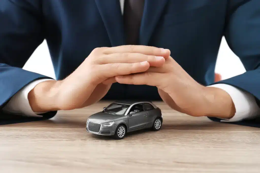 Homme protégeant une voiture miniature avec ses mains symbolisant une assurance auto